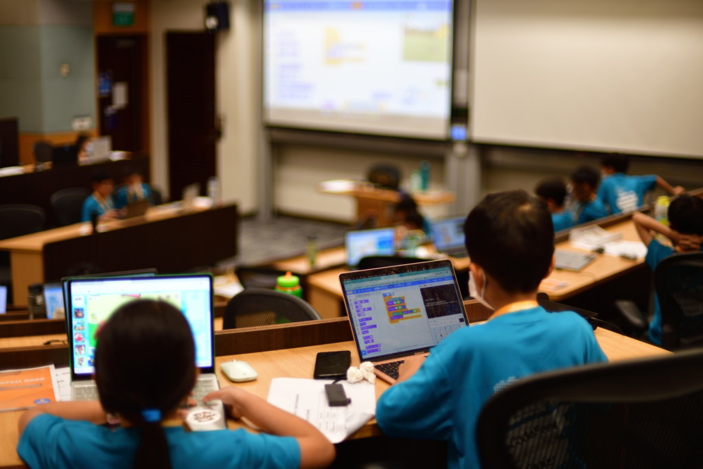 Students in blue shirts learning block-based programming on laptops during CodeFest 2022 at SMU, organized by Roboto.