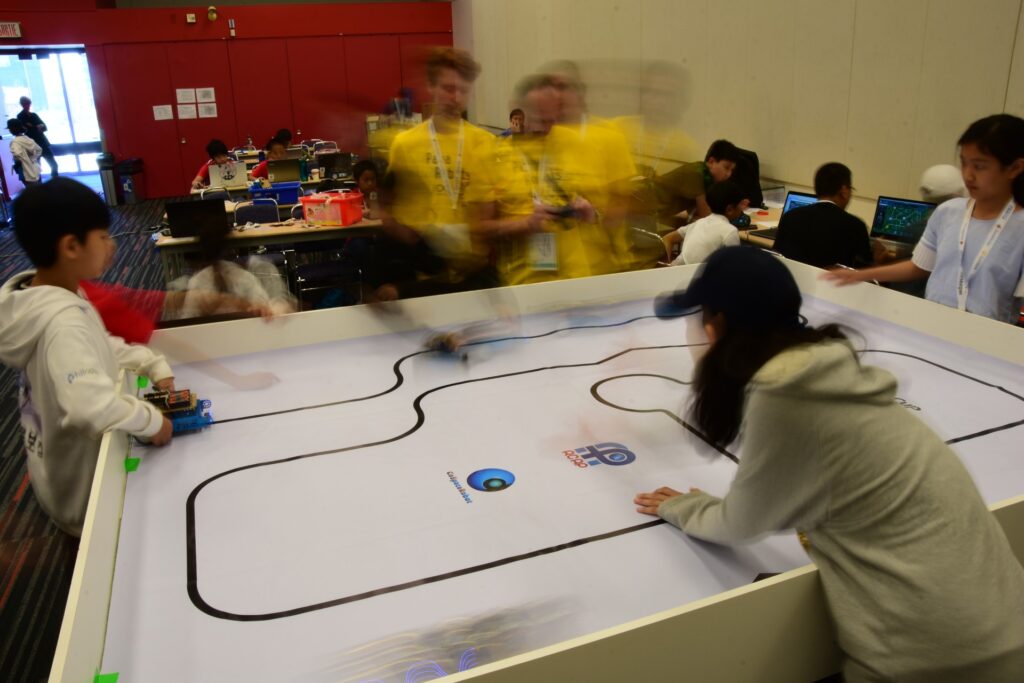 Students programming autonomous vehicles on a white track during RoboCamp at RoboCup 2018 in Montreal.