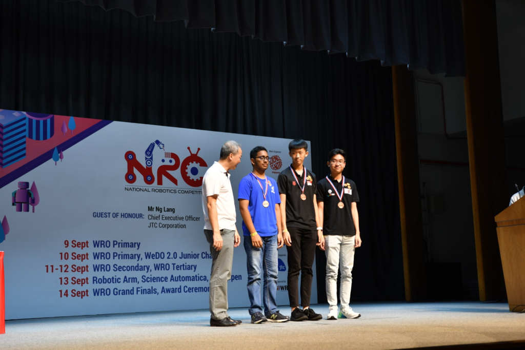 Award ceremony at NRC 2019 held at Jurong Town Hall, with student medalists and guest of honour on stage.
