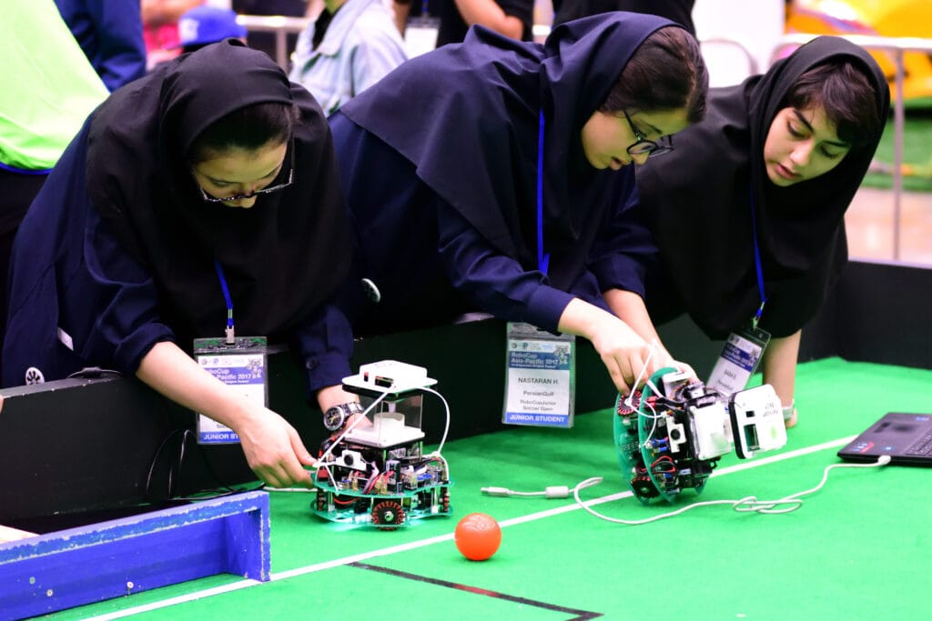 Students preparing autonomous soccer robots on a green field during RoboCup Asia-Pacific 2017, Junior Soccer Open category.